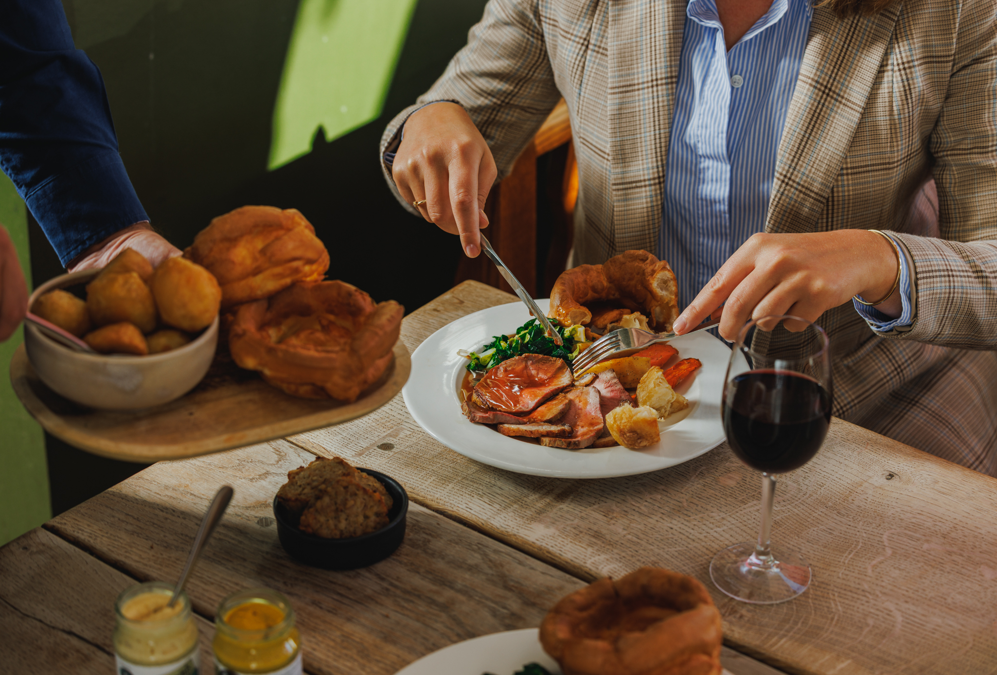 A woman eating a Sunday Roast with a glass of red wine